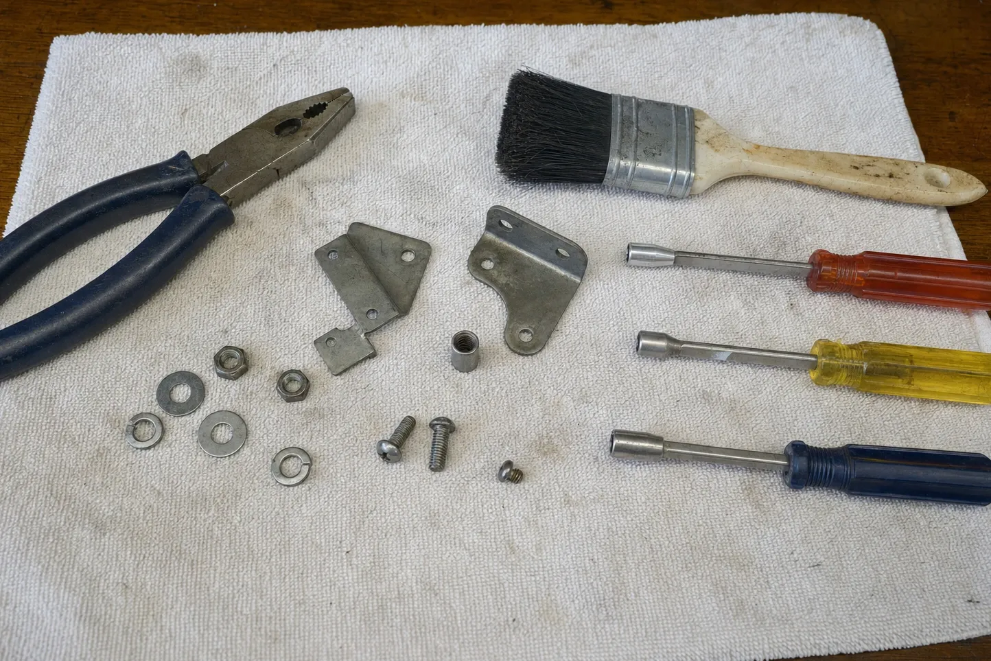 Pliers, a parts brush, three nut drivers, two stamped steel brackets and loose fixings laid out on a cloth